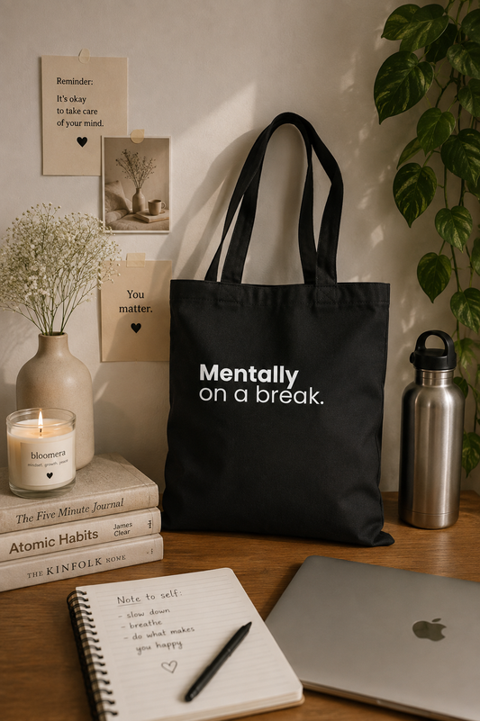 Black canvas tote bag with "Mentally On a Break" statement design styled with books, a laptop, and neutral decor