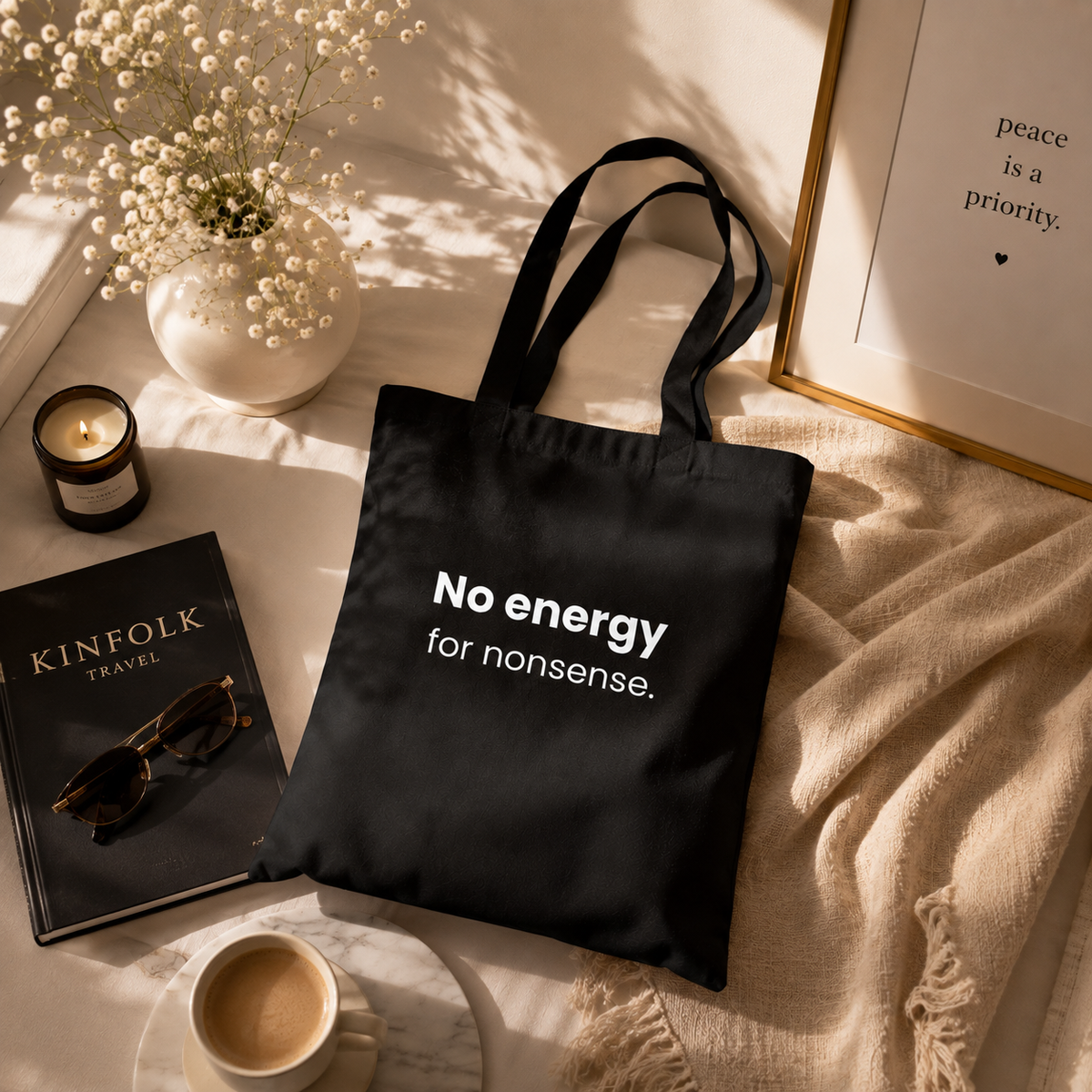 Black canvas tote bag with "No energy for nonsense" slogan styled with coffee, books, and neutral decor